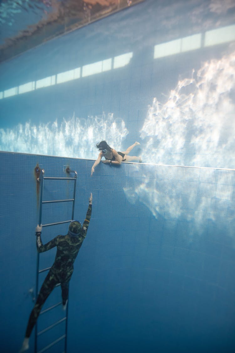 Anonymous Couple Swimming Underwater In Pool Near Hole