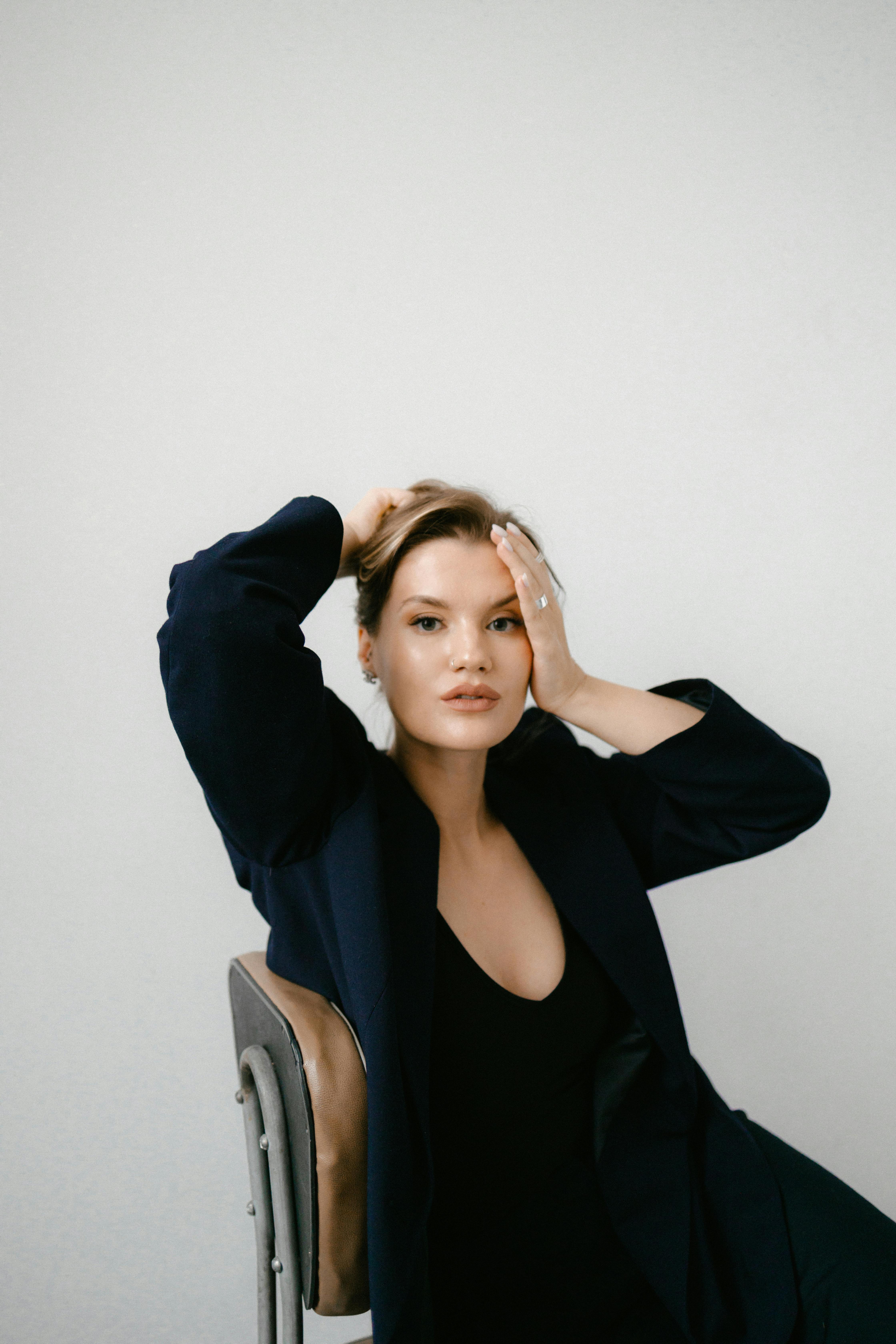 Portrait of a stylish woman sitting and posing with hand on face in a studio setting.