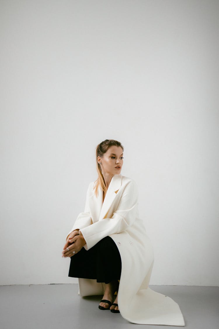 Woman In White Coat Squatting Near White Wall