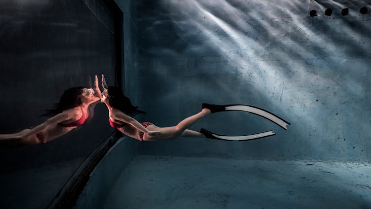 Woman In Fins Swimming In Pool With Glass Wall