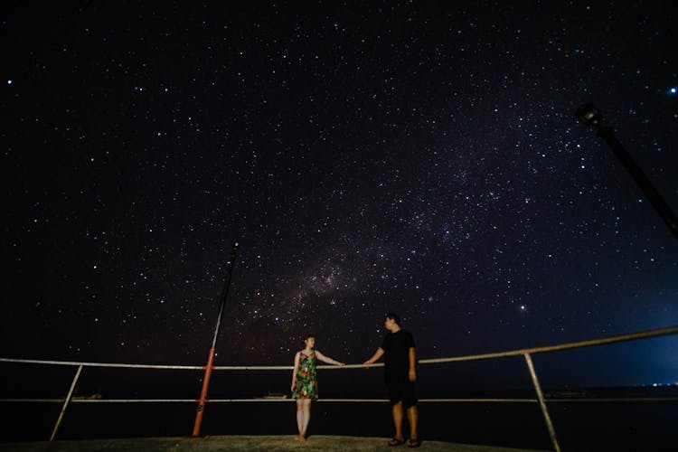 Couple On Viewpoint Near Railing Under Starry Sky At Night