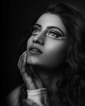 Artistic black and white portrait of a woman with eye makeup, looking thoughtfully upward.