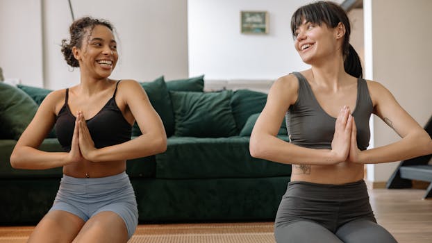 Two women practicing yoga indoors, in sync, smiling at each other.