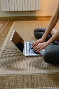 A woman practices yoga at home while using a laptop for guidance.