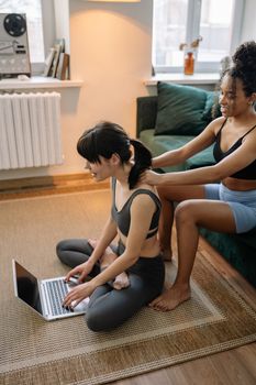 Two women engaged in home yoga session while using a laptop, promoting connection and health.