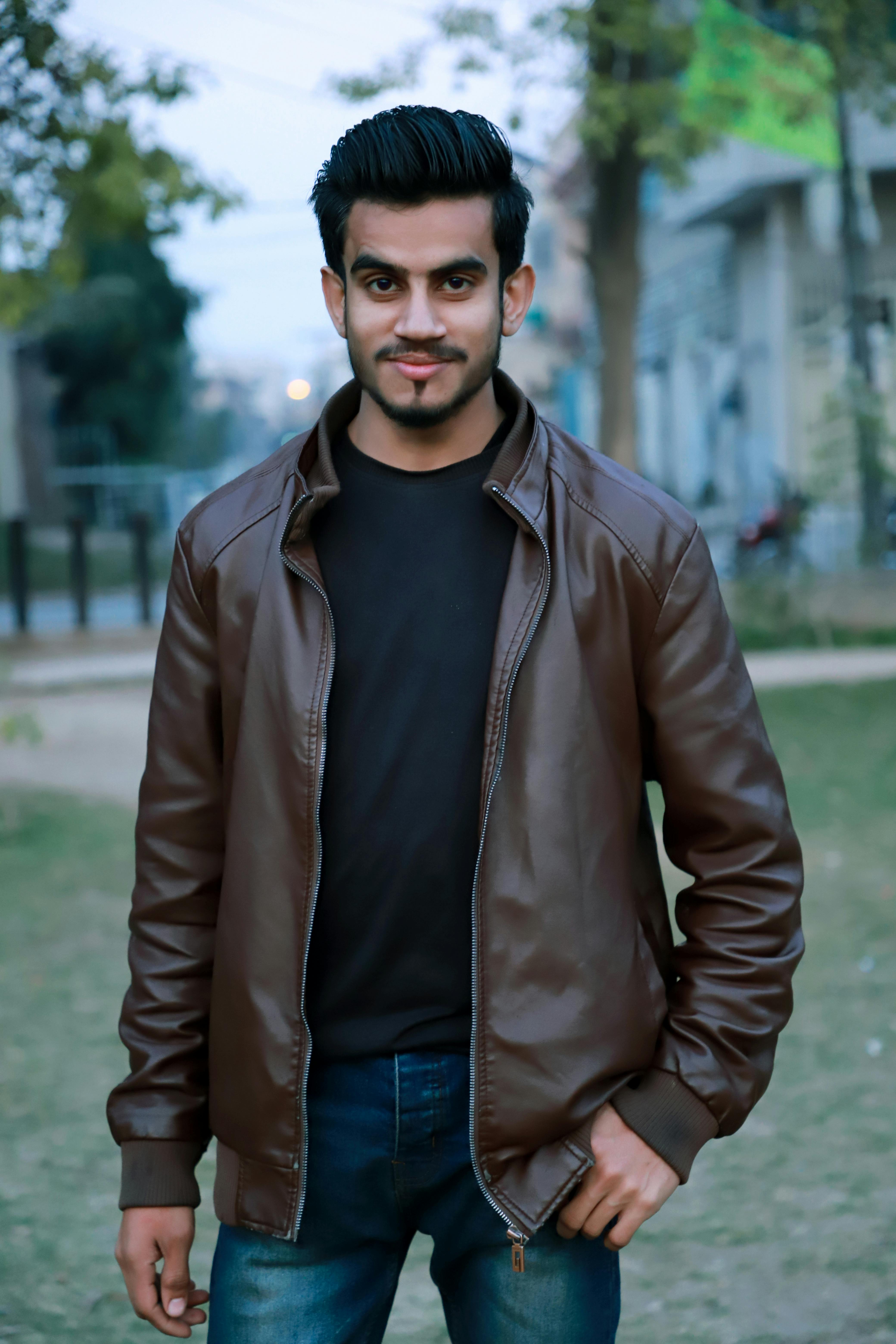 Stylish young man in brown leather jacket posing confidently outdoors in Lahore park.