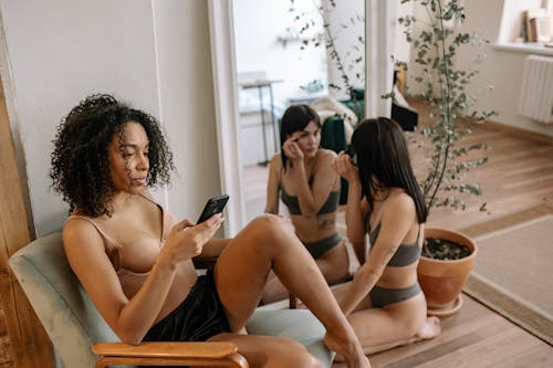 Young Woman Texting Sitting Next to Her Girlfriend Applying Mascara