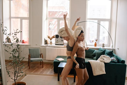 Two women with towels dance joyfully in a bright living room, showcasing happiness and harmony.