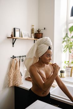 African American woman practicing self-care by brushing teeth in a contemporary bathroom setting.