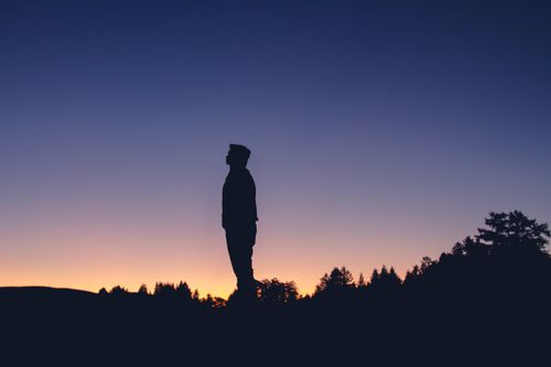 Free A lone figure stands silhouetted under a colorful sunset sky, evoking solitude and introspection. Stock Photo