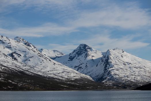 Stunning view of snow-covered peaks and calm lake under a clear sky in Tromsø, Norway.