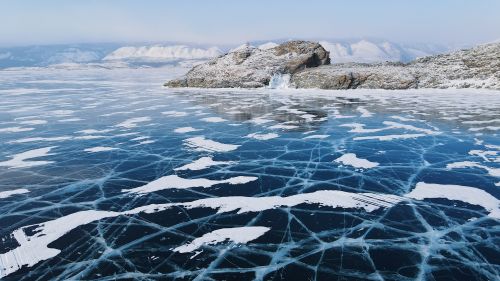 Free Captivating winter scene of Lake Baikal's cracked ice surface with snowy mountains in the background. Stock Photo