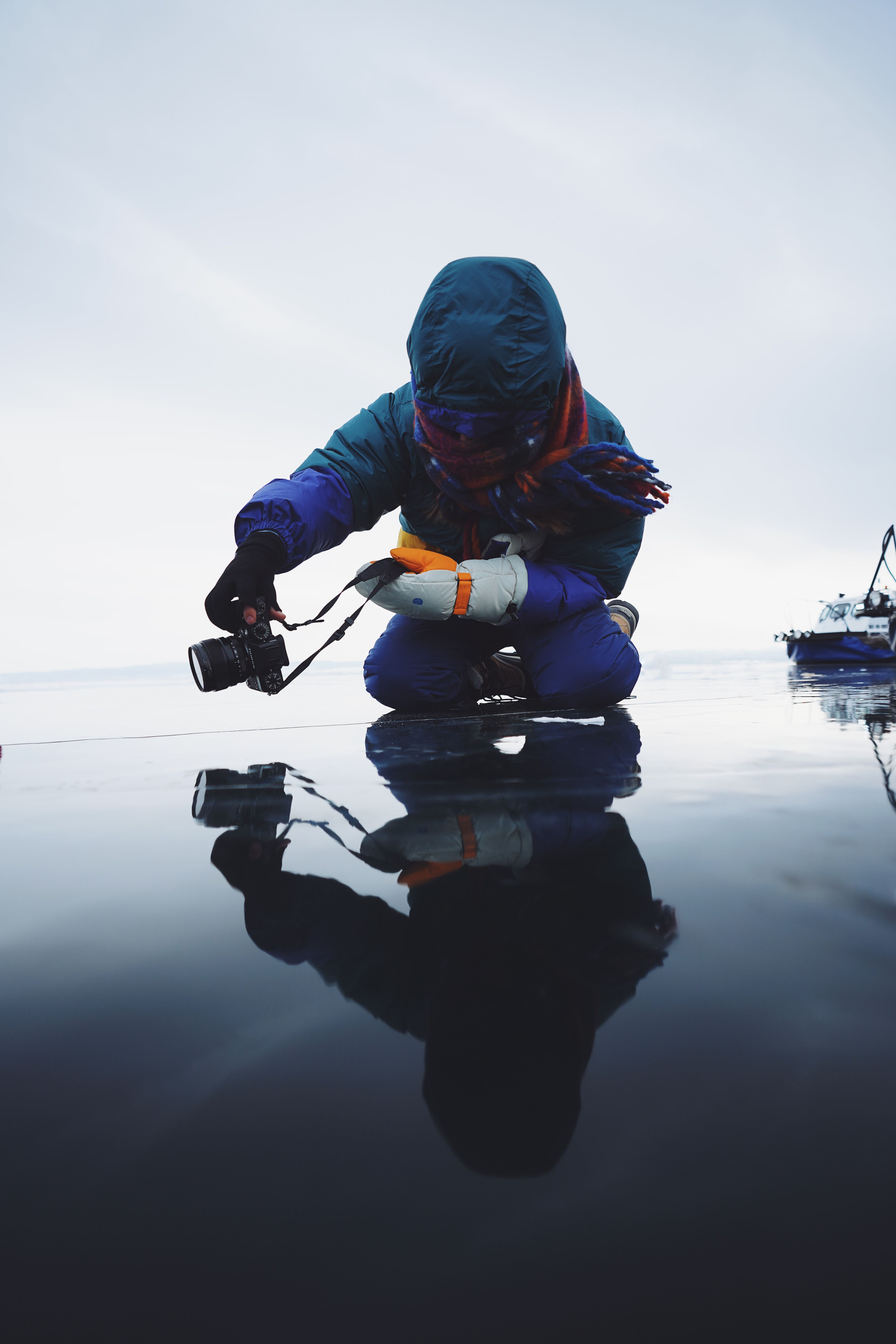 Free A photographer in winter clothing capturing reflection on a frozen lake with a camera. Stock Photo