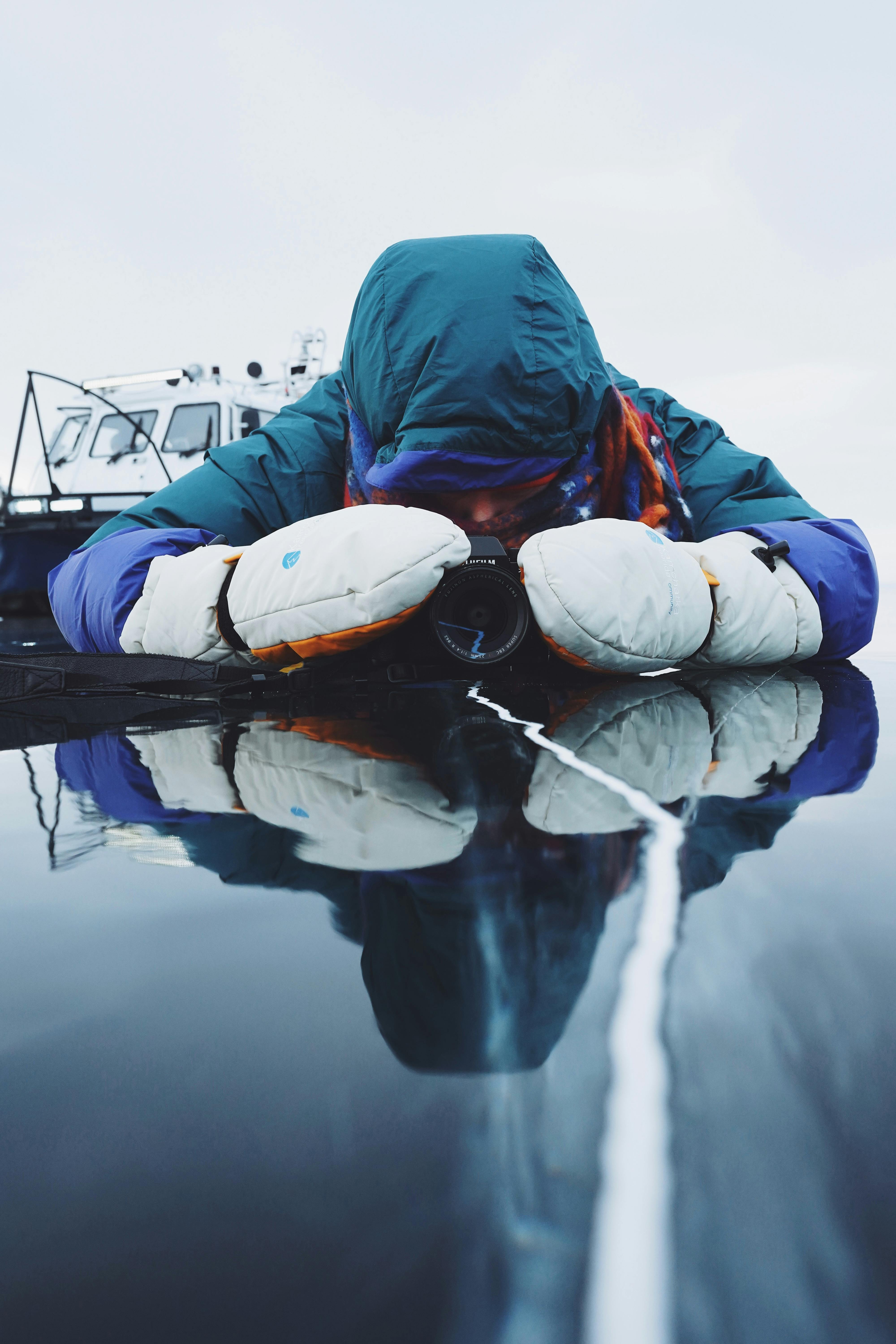 A person in winter clothing photographs reflections on frozen Lake Baikal.