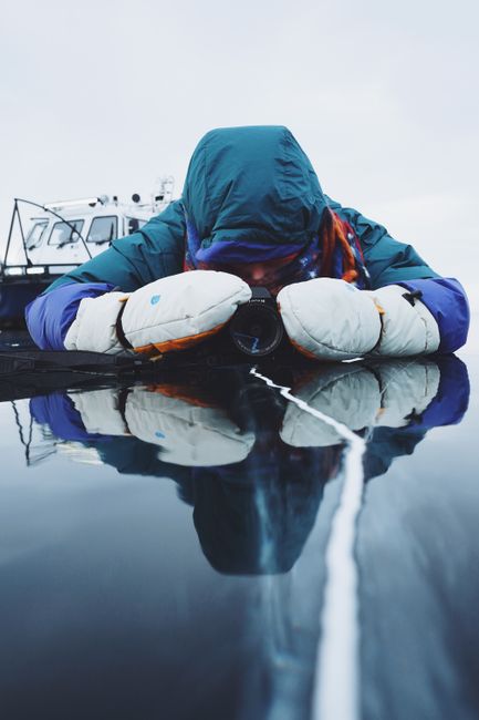 A person in winter clothing photographs reflections on frozen Lake Baikal.