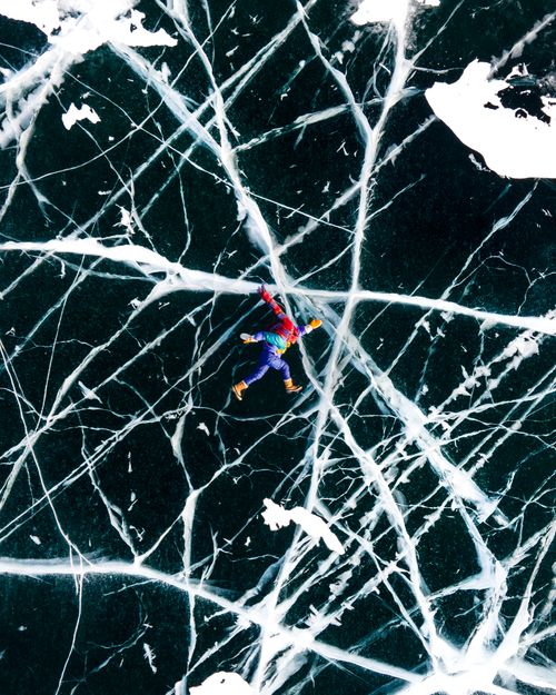 Free Vibrant aerial view of a person lying on the cracked ice of Lake Baikal, Russia. Stock Photo