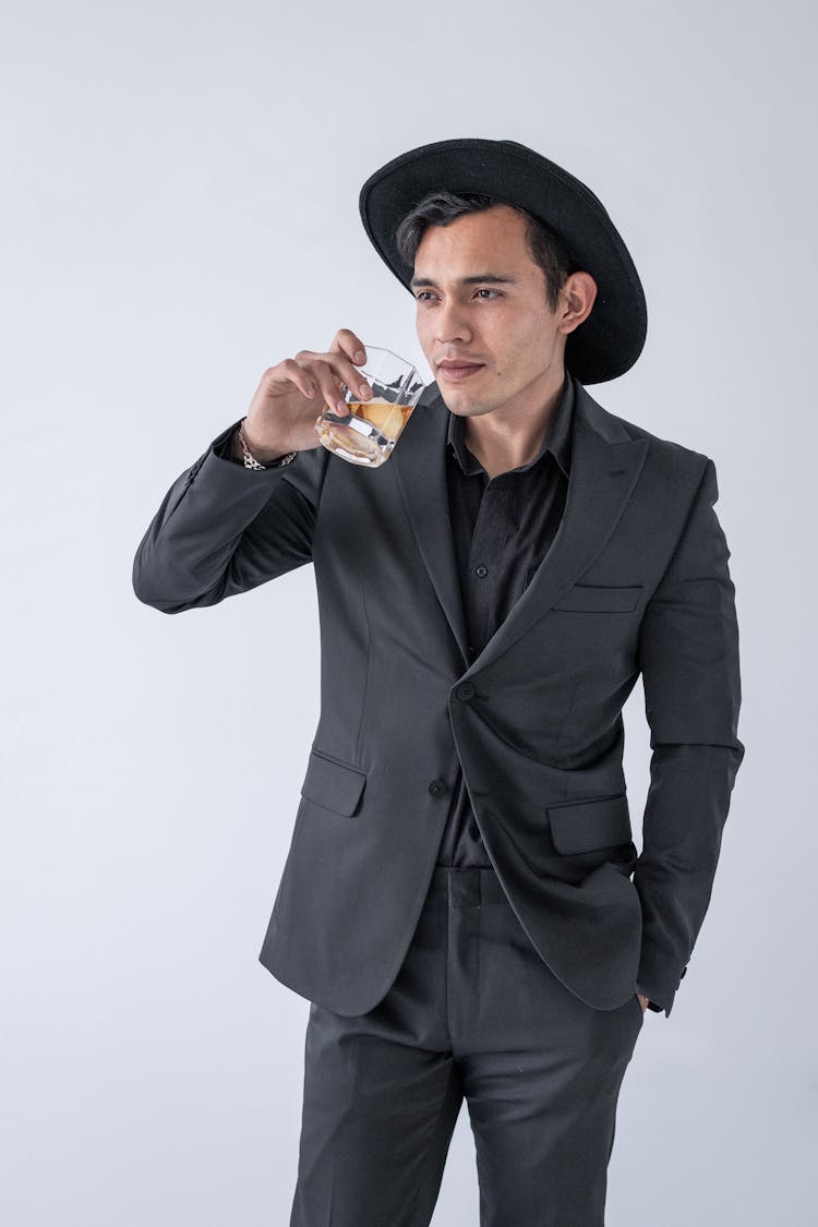 Portrait Of A Man Wearing Dark Suit And Hat Drinking Alcohol From A Glass