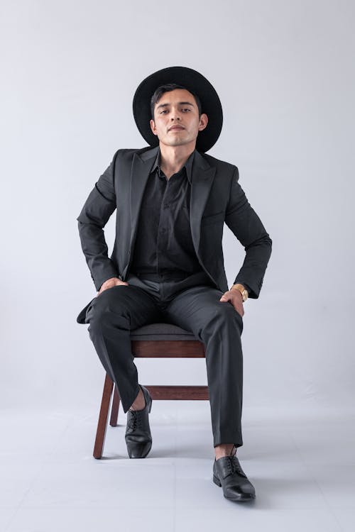 A Man in Black Suit and Hat Sitting on a Chair