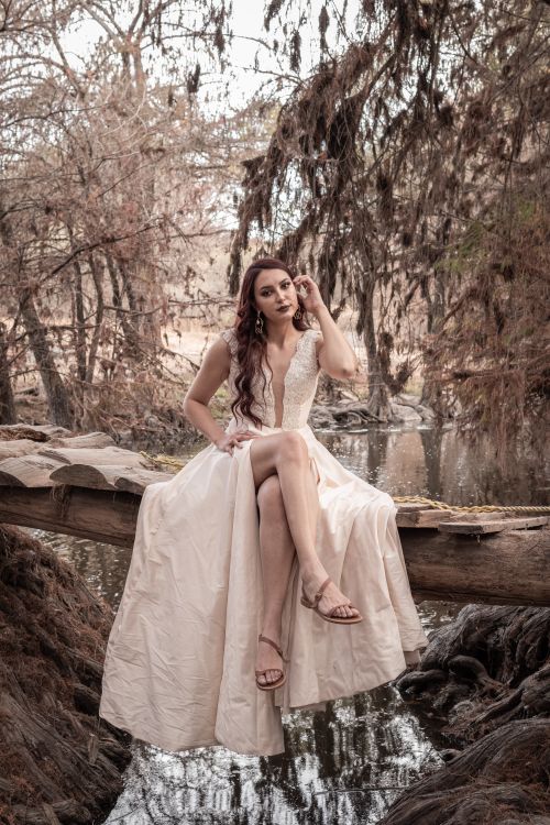Free A woman in a white dress sitting elegantly on a rustic wooden bridge in a serene forest setting. Stock Photo