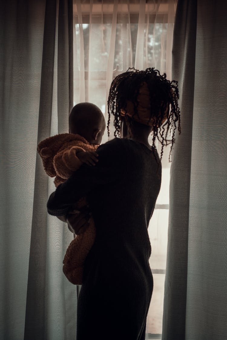 A Mother Carrying Her Child While Looking Outside The Window