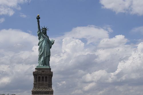 Free View of the iconic Statue of Liberty with a vibrant blue sky background, symbolizing freedom. Stock Photo