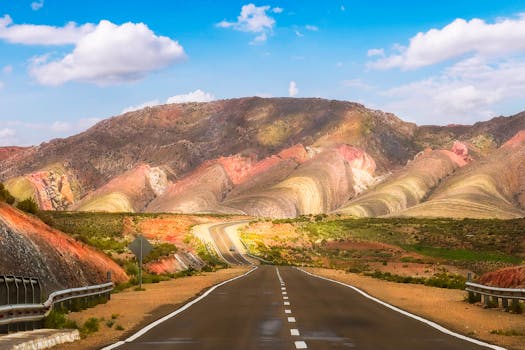 A scenic drive on a winding road through vibrant multicolored mountains under a bright blue sky.