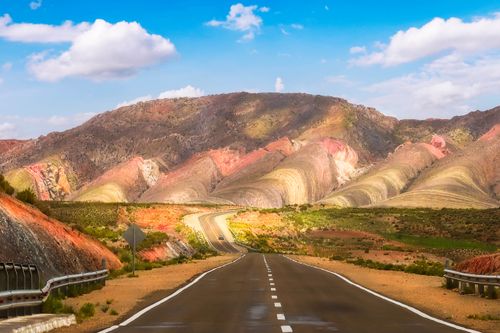 Free A scenic drive on a winding road through vibrant multicolored mountains under a bright blue sky. Stock Photo