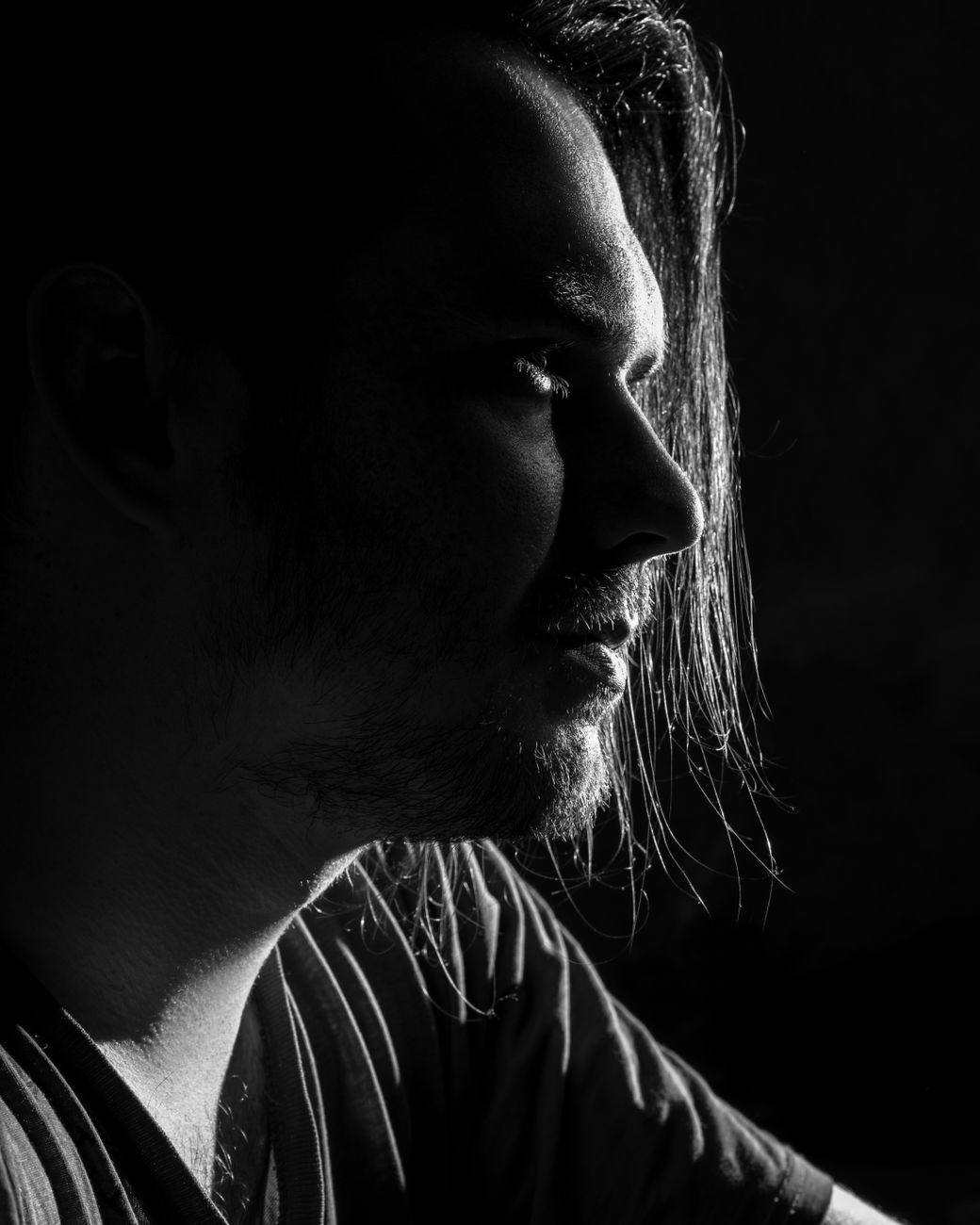 A thoughtful black and white side profile portrait of a man with dramatic lighting.. thoughtful, black, white