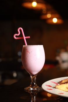 A tempting strawberry milkshake in a glass with a coiled straw on a restaurant counter.