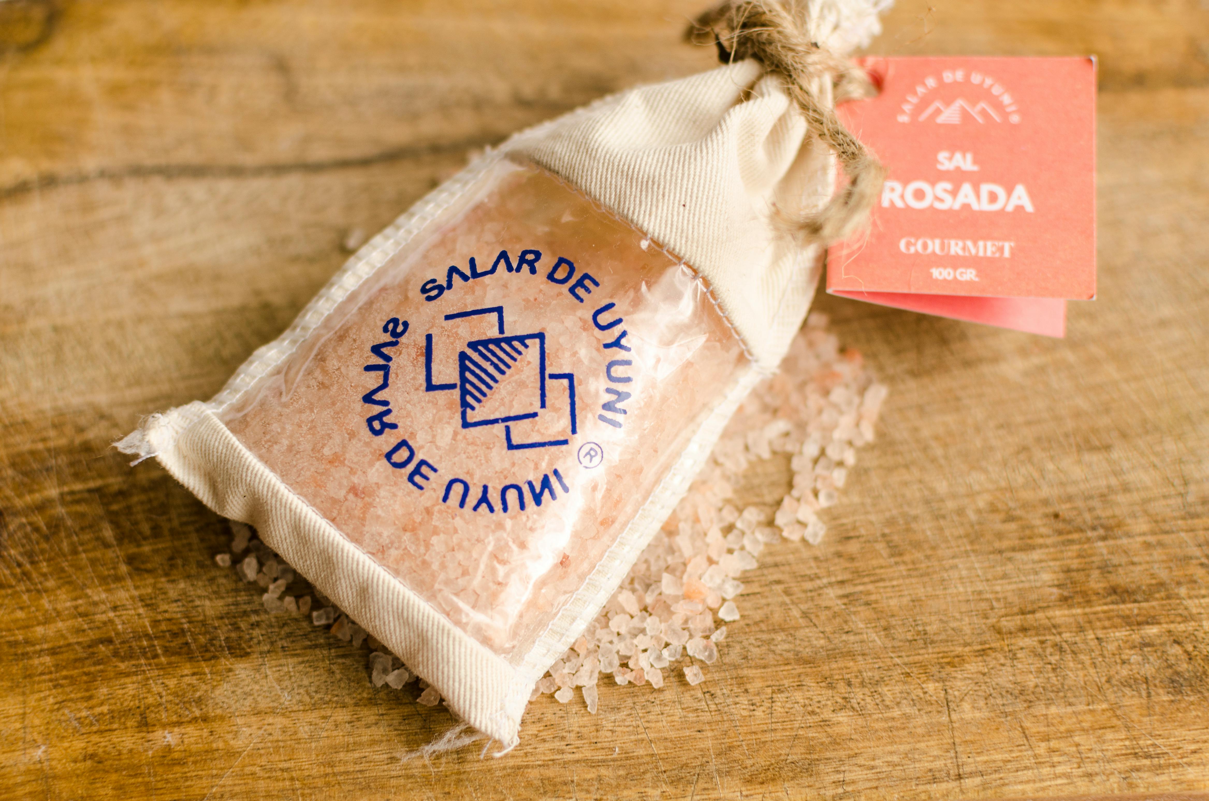 Close-up of gourmet pink salt from Salar de Uyuni in a fabric pouch, displayed on a wooden surface.