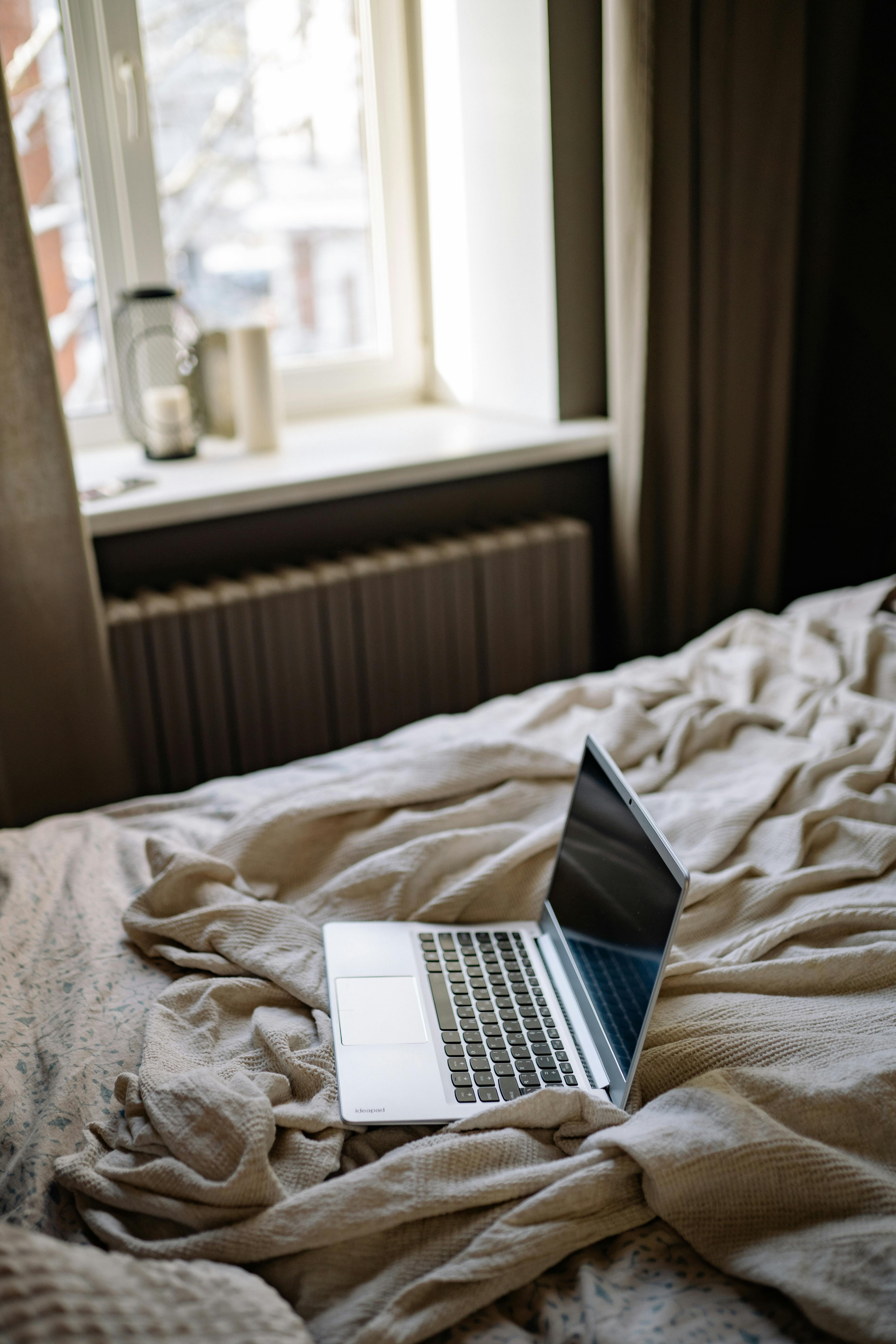 open laptop on a bed with creased beige blanket