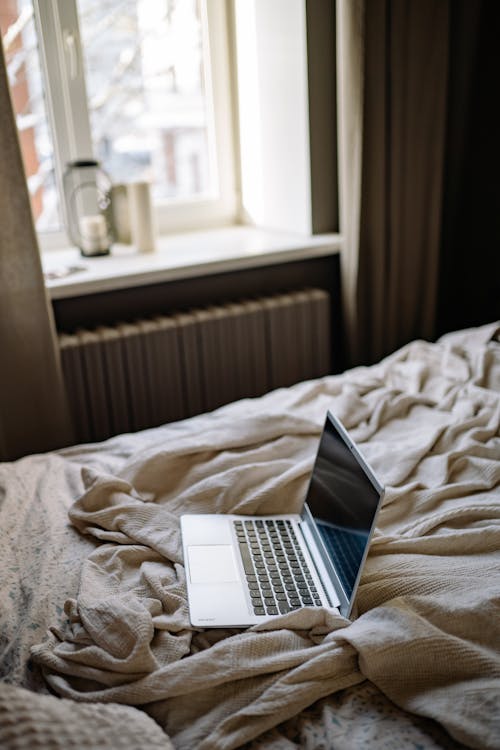 Open Laptop on a Bed with Creased Beige Blanket