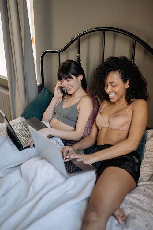 Woman in Black Tube Top and Black Shorts Sitting on Bed Using Macbook