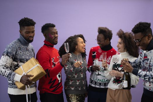 Joyful group of adults celebrating with champagne in festive sweaters during a holiday party.