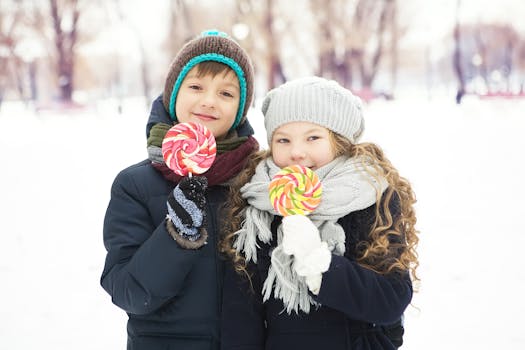 Two warmly dressed children enjoying colorful lollipops in a snowy winter park.
