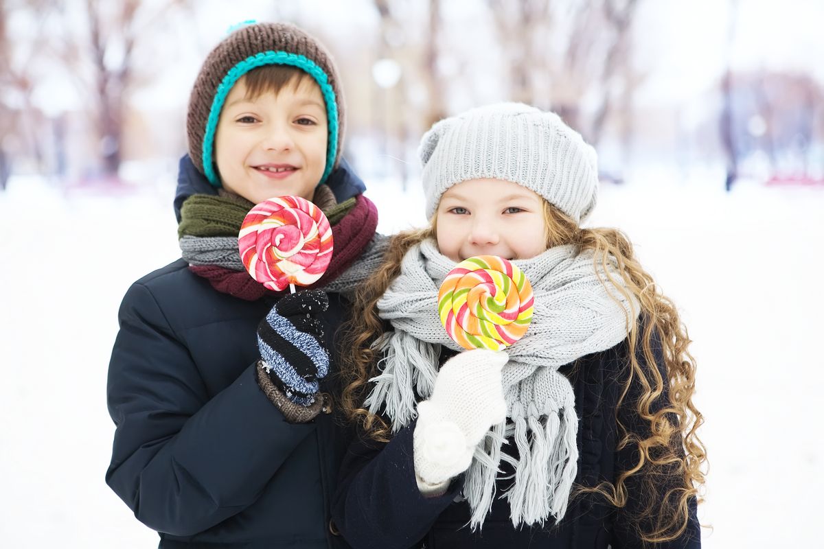 Children bundled up in winter clothing enjoy colorful lollipops outdoors on a snowy day.