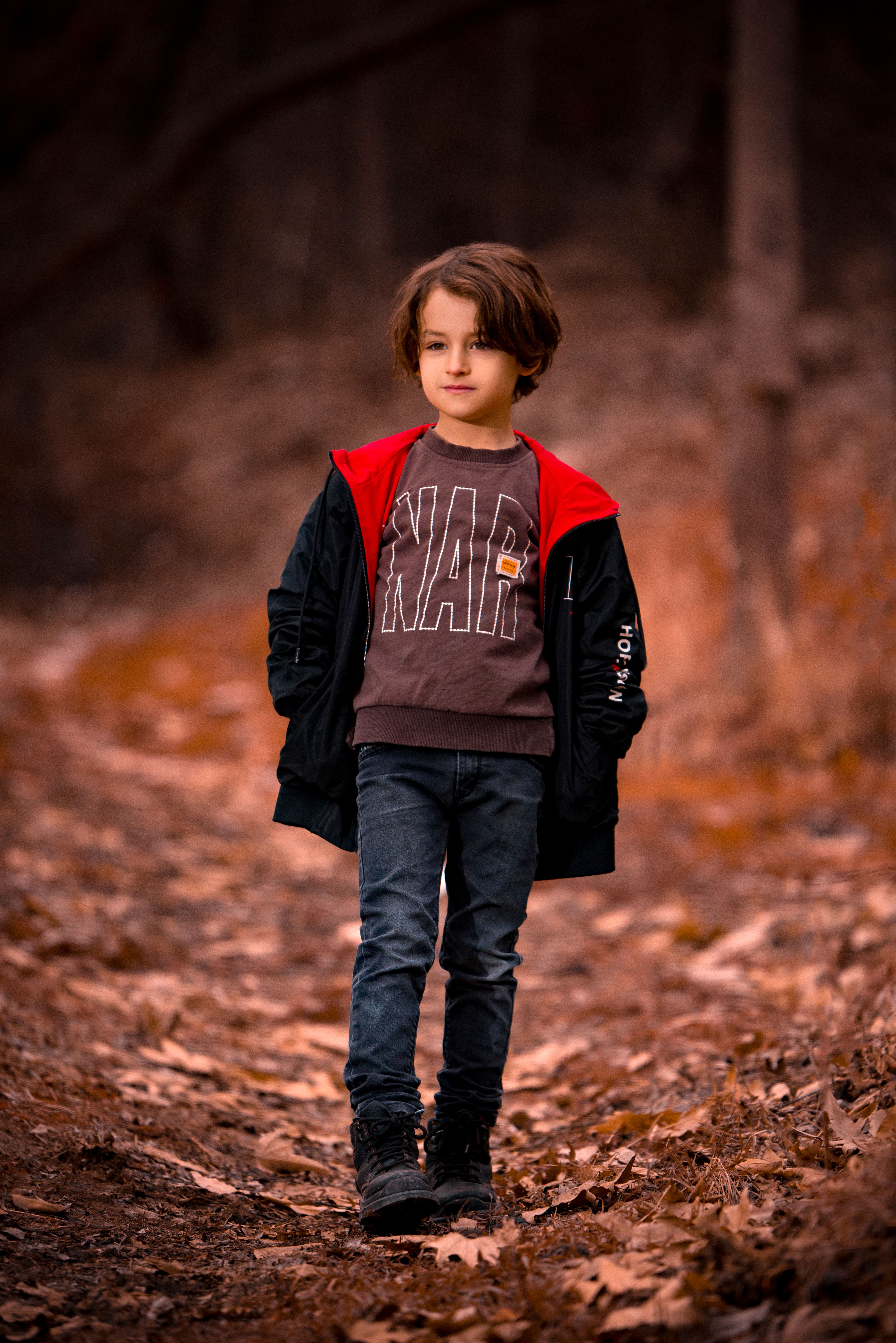 A young boy walking on a leaf-covered path in an autumn forest