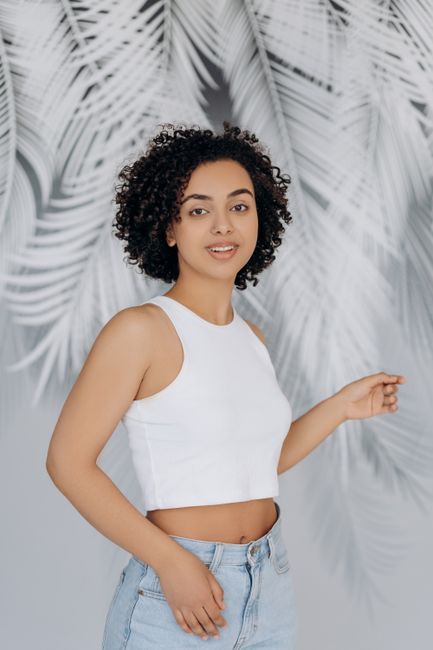 Portrait of a woman with curly hair and fresh style posing in a studio.