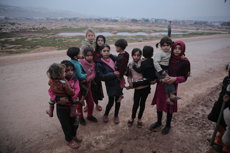 Group Of Young Children Standing On An Unpaved Muddy Road 