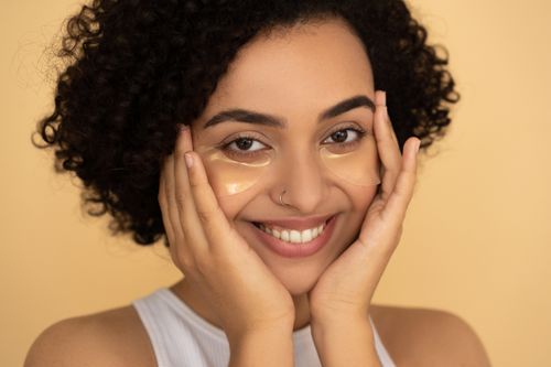Free Close-up portrait of a smiling woman with under eye patches showcasing skincare routine. Stock Photo