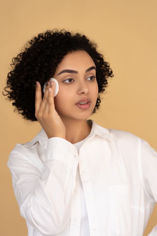 Free A woman with curly hair applying facial skincare in a studio setting. Stock Photo