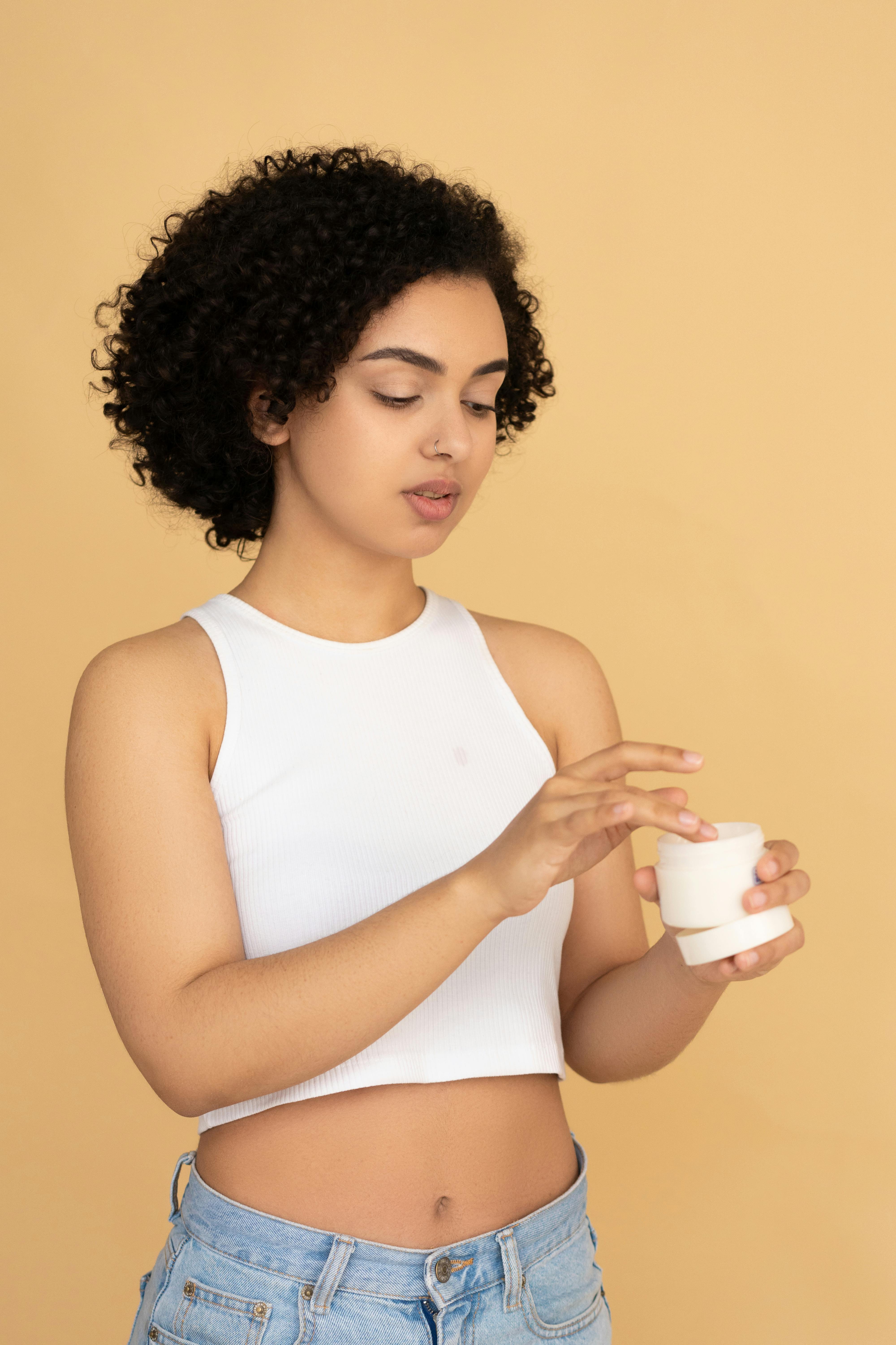 woman in white tank top holding a beauty cream