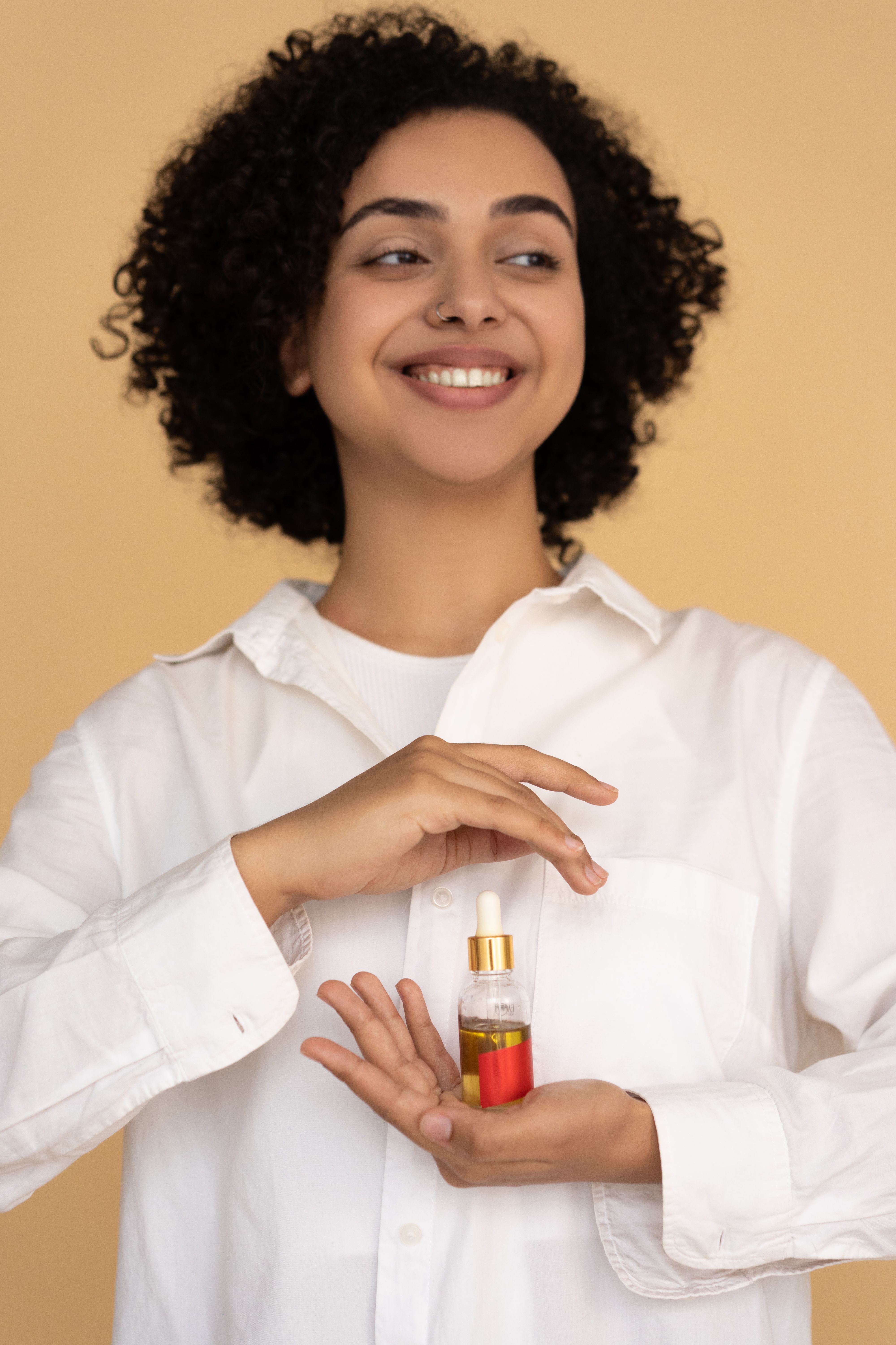 Cheerful woman presenting a bottle of natural herbal hair care oil in a studio
