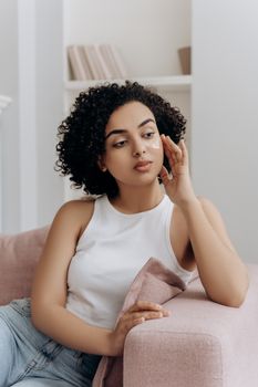 Chic young woman with natural curls relaxing indoors, embodying modern lifestyle and beauty.