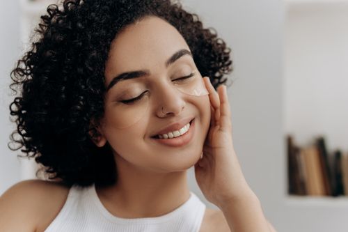 Free Young woman smiling gently with under eye patches indoors. Stock Photo