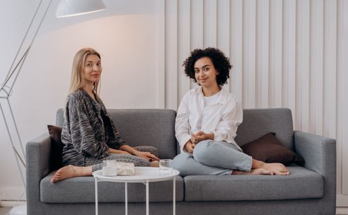 Free A scene of two women enjoying a comfortable moment on a stylish sofa in a well-lit room. Stock Photo