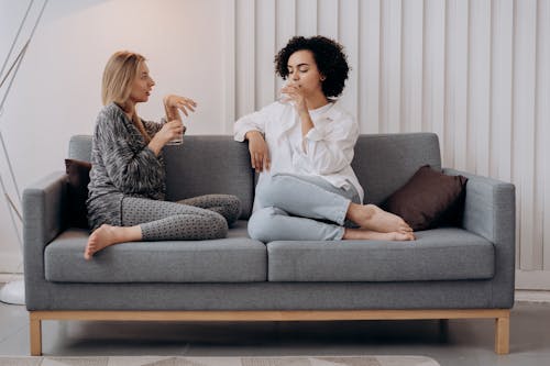 Two Women Sitting On A GRay Couch Drinking Water