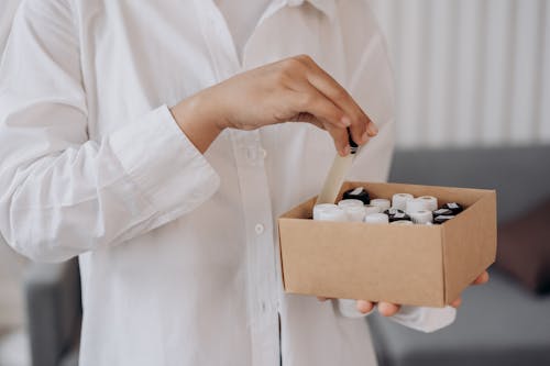 Free Person in White Dress Shirt Holding Brown Box With Bottles Of Essential OIl Stock Photo