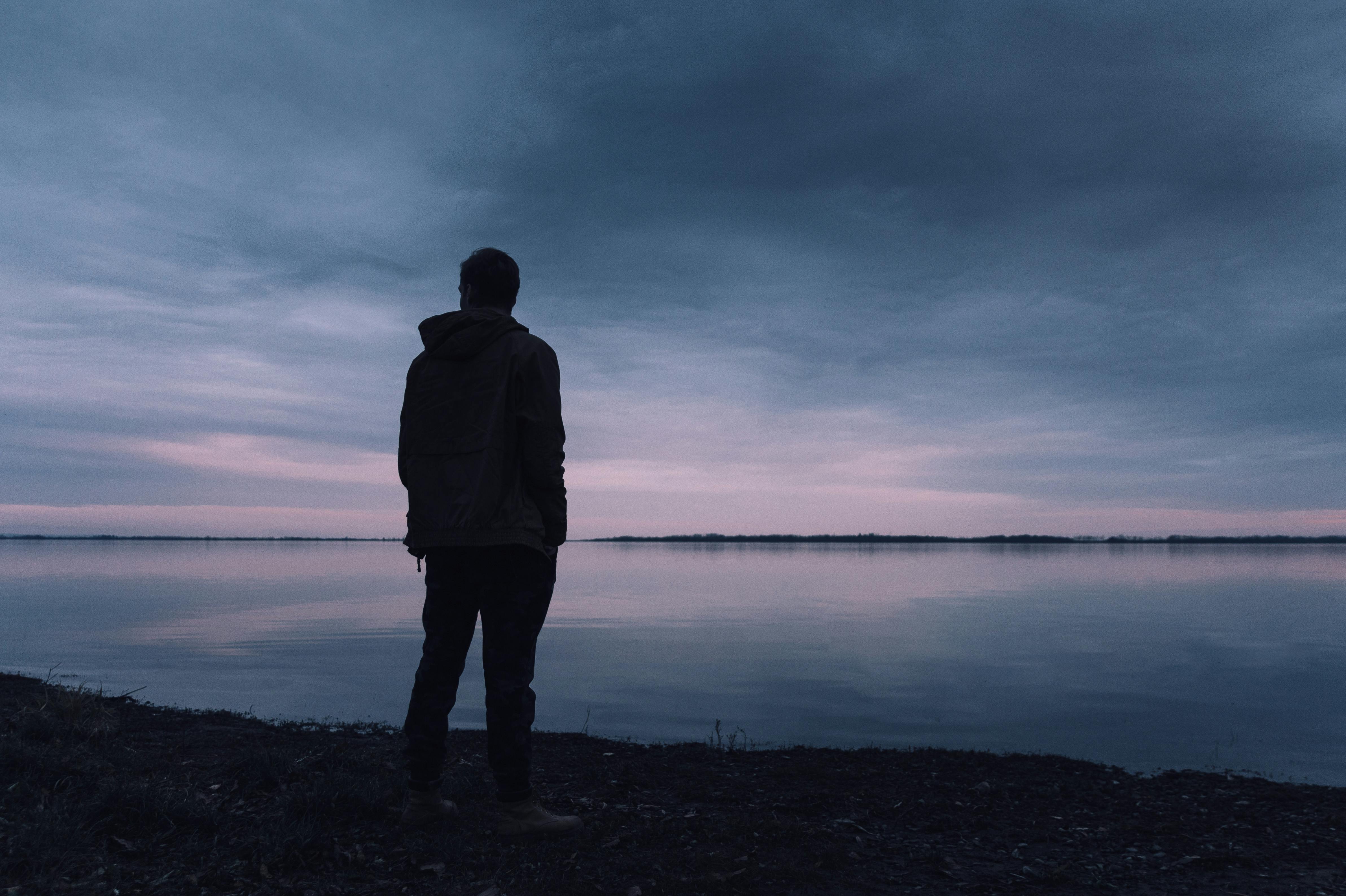 Man thinking while standing near a lake. | Photo: Pexels