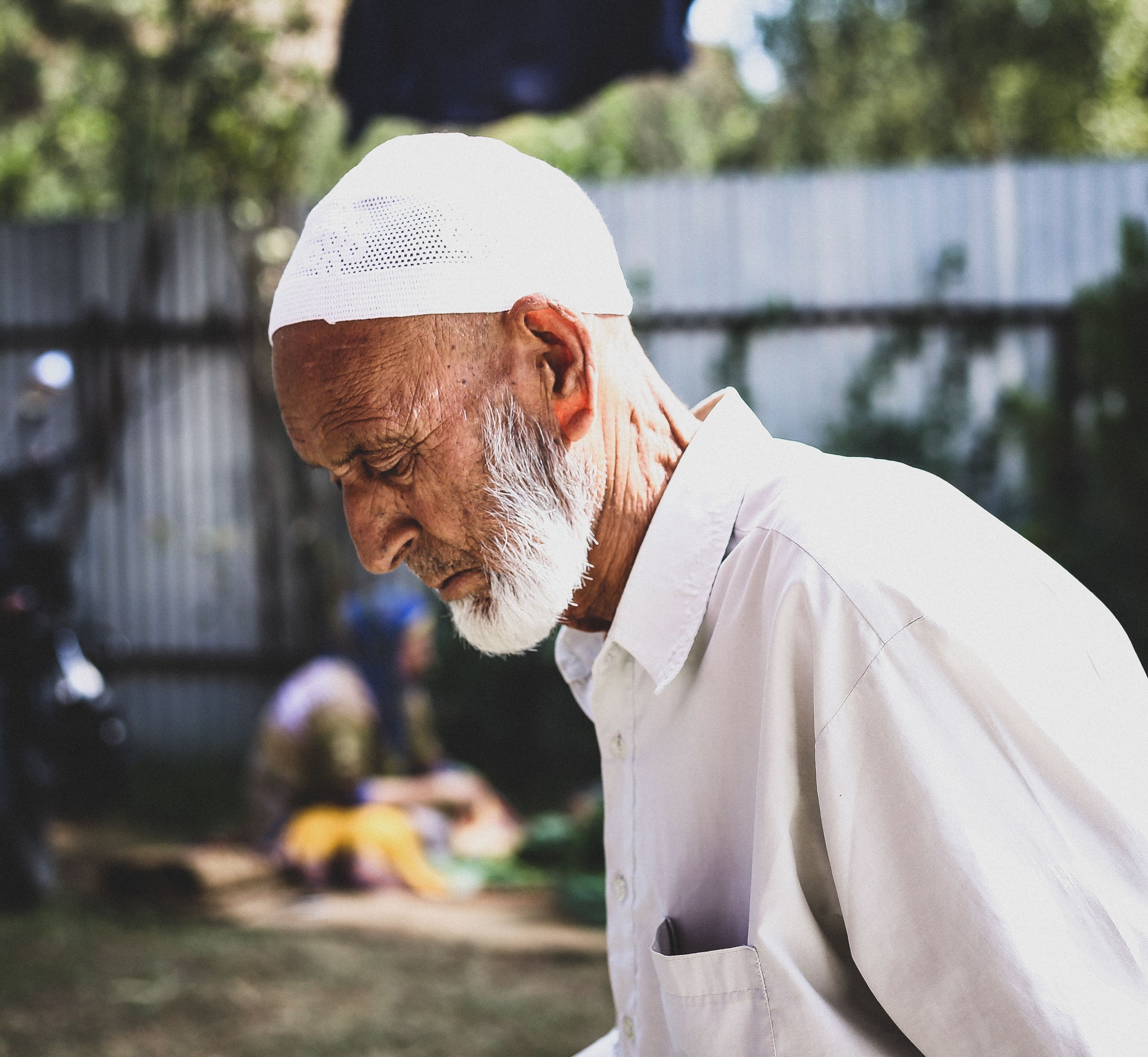 Side profile of an elderly man wearing a kufi outdoors, captured in a moment of contemplation.